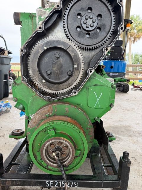 A green John Deere industrial engine block mounted on a metal stand, showcasing the exposed front gear train and crankshaft.