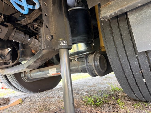 A low-angle view of a vehicle's underside, showing a pneumatic leveling jack lowered toward the ground near a rear tire.