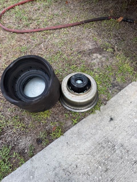 A disassembled air suspension bag and its metal base component lying on grass next to a concrete walkway.