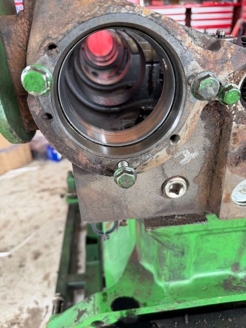 Close-up of a greasy, metallic engine block part with a central circular opening and green-painted bolt heads.