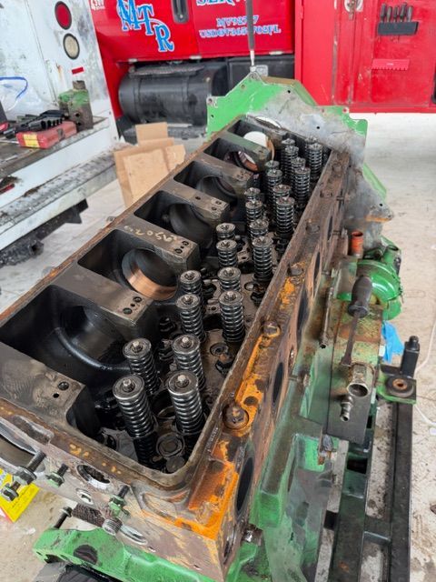 A partially disassembled green industrial engine sits in a shop, showing exposed valve springs and internal components.