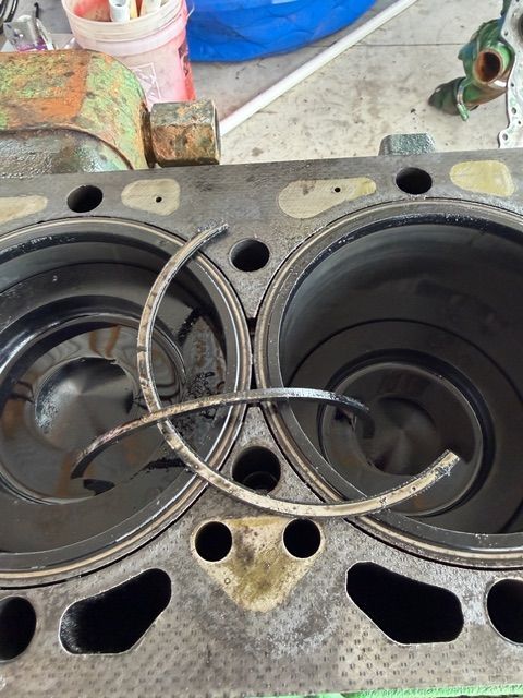 A broken metal piston ring sits on top of two open engine cylinders in a dirty, dismantled engine block.