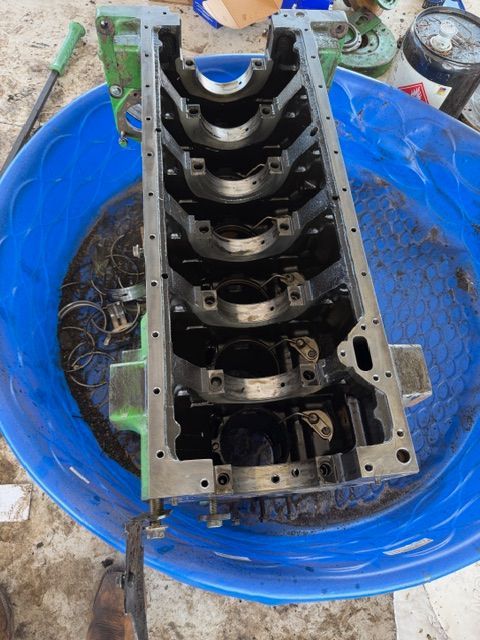 An engine block rests inside a blue plastic tub on a workshop floor.