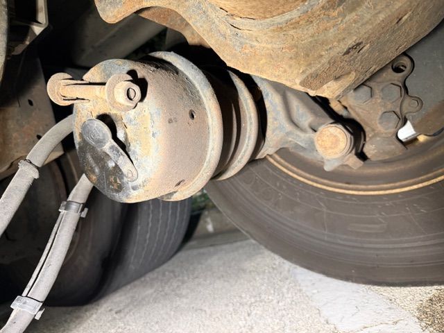 A rusty, cylindrical air brake chamber attached to the axle assembly of a heavy-duty truck wheel.