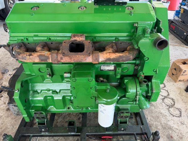 A bright green John Deere industrial diesel engine with a rusted exhaust manifold, mounted on a metal transport stand.