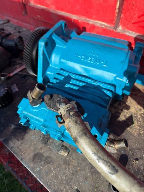 A bright blue automotive water pump with a gear, metal hoses, and clamps sitting on a metal workbench.