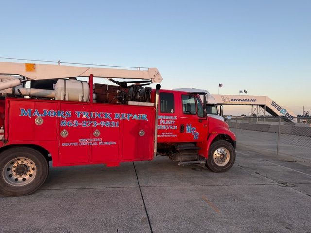 A red Majors Truck Repair service truck parked on a paved lot at sunset with a pedestrian bridge in the background.