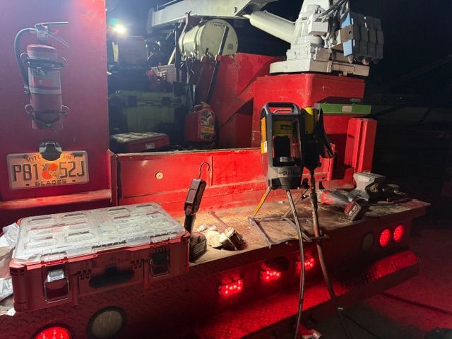 A red utility truck bed at night, featuring a mounted crane, a fire extinguisher, tools, and a license plate PB1 52J.