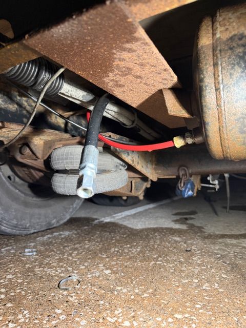 An undercarriage view showing a disconnected black hydraulic hose hanging near a red line connected to a metal tank.