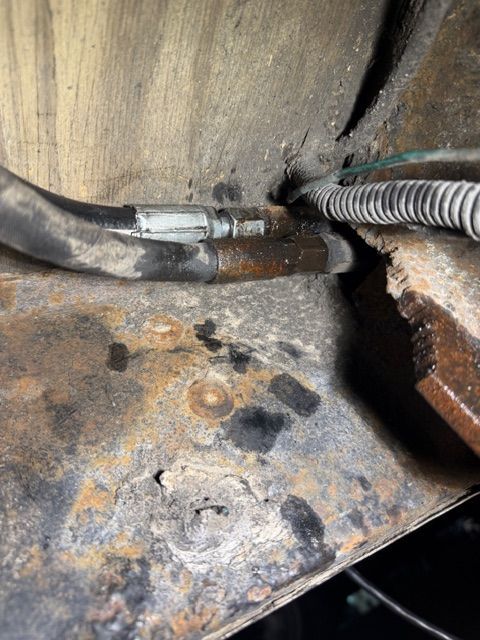 A close-up view of two dark hydraulic hoses and a corrugated electrical conduit mounted against a rusted metal frame.