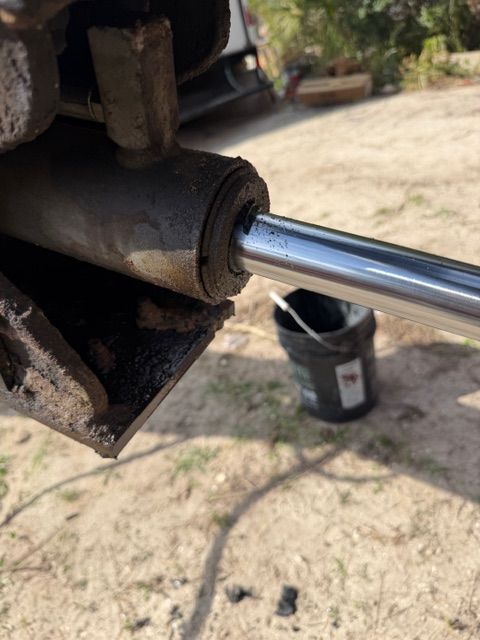 Close-up of a shiny metal piston rod extending from a rusted hydraulic cylinder outdoors.