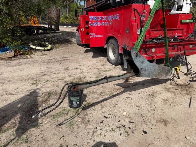 Red street-cleaning truck with hoses on a dirt path near a wooded area
