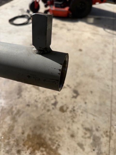 Close-up of a black metal tube with a small upright bracket on top, outdoors on concrete.