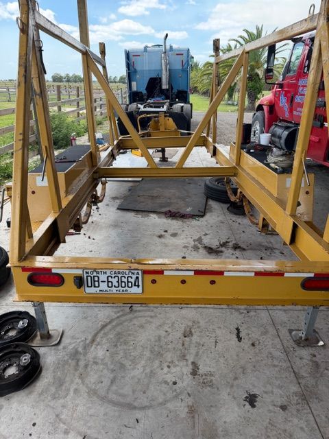 Yellow metal trailer with a blue tractor and red truck in a yard