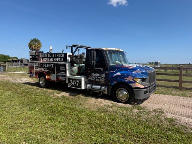 Blue-and-black food truck parked on a dirt road beside a fence under a clear sky