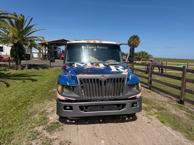 Blue truck parked on a dirt path beside a wooden fence and palm tree under a clear sky.