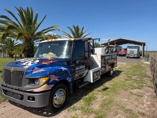 Blue tow truck parked on grass near palm trees under a clear sky