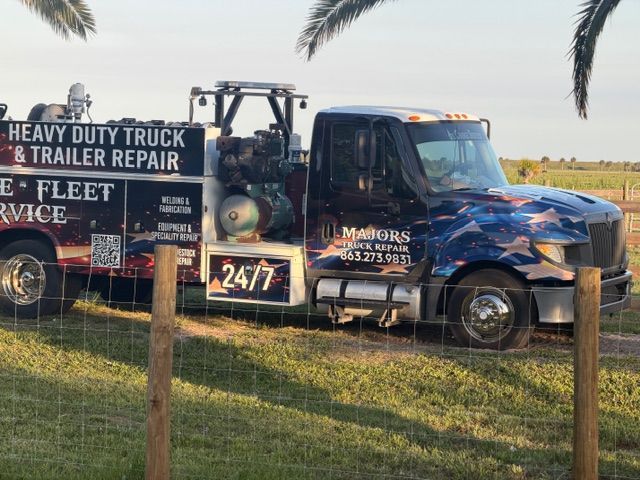 Heavy-duty truck and trailer repair service truck parked on grass with business signs and 24/7 branding