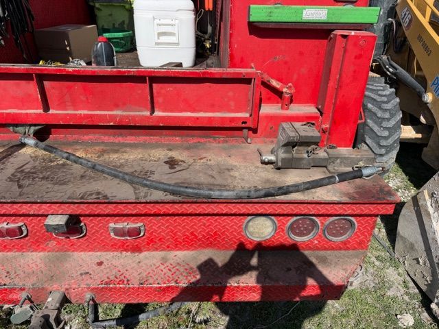 Red utility trailer bed with worn black mat, red rails, and circular rear lights outdoors on grass