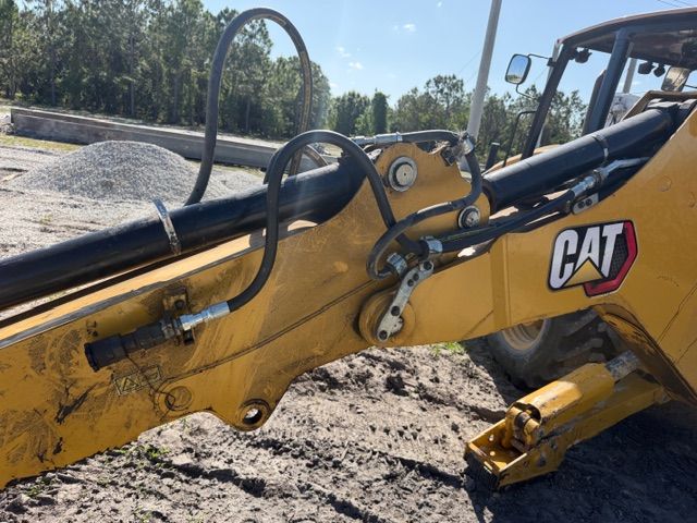 Close-up of a yellow CAT excavator arm and hydraulic hoses at a construction site