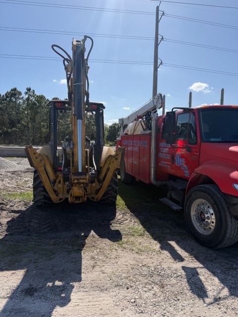 Yellow excavator beside a red utility truck on a dirt lot under a clear sky