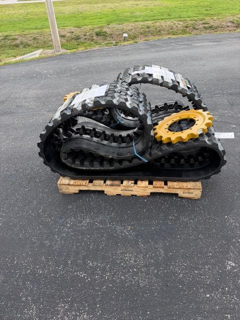 Stacked black and gray off-road tires on a wooden pallet, with one yellow wheel hub, outdoors on pavement.