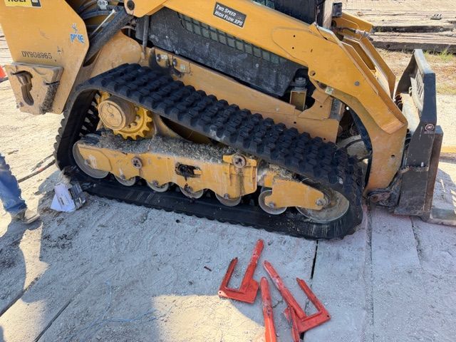 Yellow tracked skid steer stuck in cracked pavement beside red plastic pieces