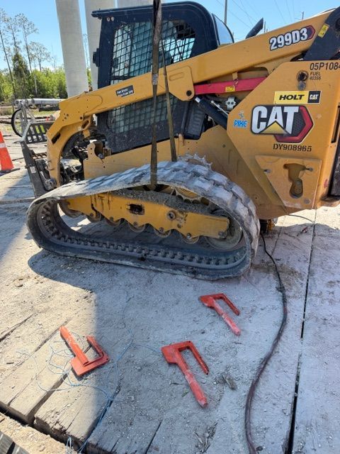 Yellow CAT skid steer with damaged track on a concrete lot, maintenance tools scattered nearby