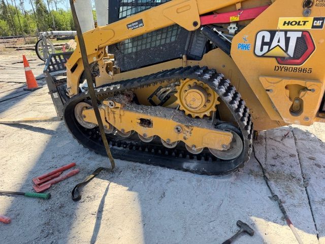 CAT skid steer with damaged track on a sidewalk beside tools and traffic cones