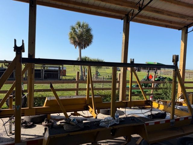 Open-air workbench with tools under a shelter, overlooking a grassy field and palm tree.
