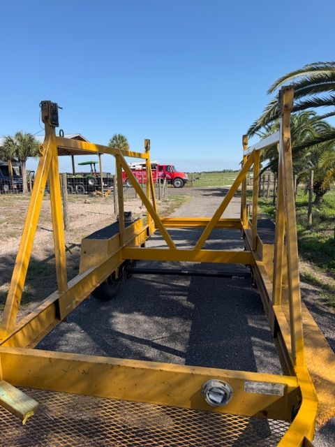 Yellow metal trailer frame on gravel lot with a red truck and palm trees in the background