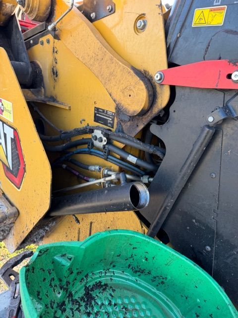 Close-up of yellow construction machinery with hoses, a red lever, and a green bucket below