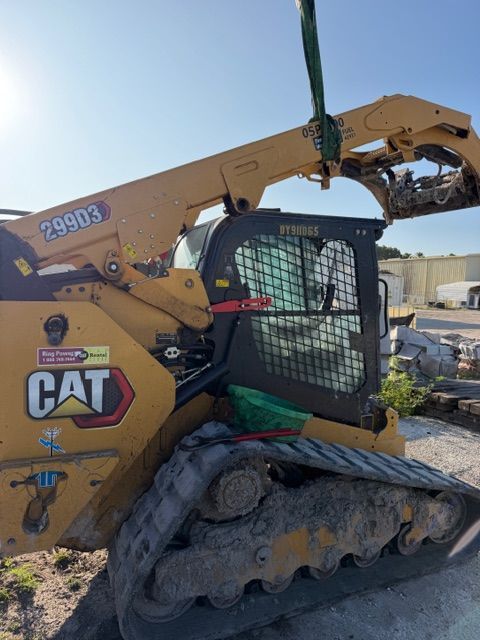 Yellow CAT skid-steer loader with a grapple attachment on a dirt lot under a blue sky