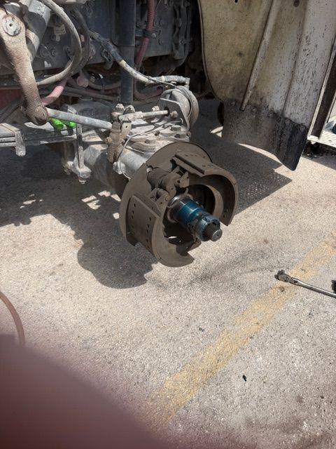 Close-up of a detached vehicle brake rotor and hub assembly on pavement near exposed suspension parts.
