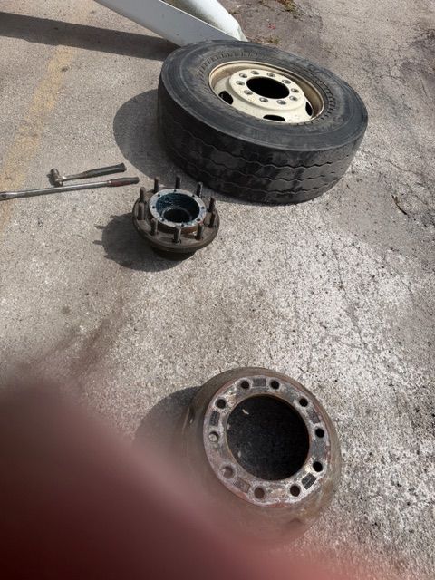Truck wheel parts and tools on concrete, including a tire, hub assembly, and metal rim.