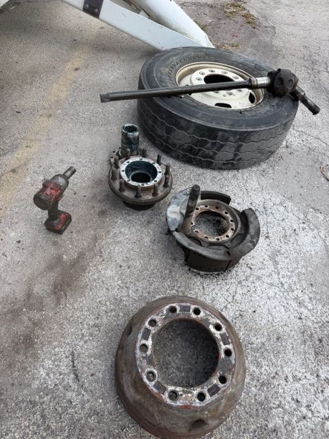 Disassembled car wheel hub and brake parts on concrete beside a tire and jack
