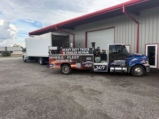 Tow truck with colorful advertising parked beside a warehouse on a gravel lot