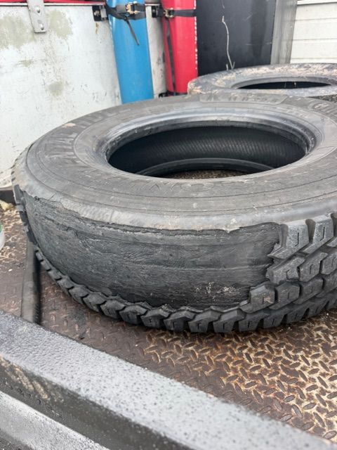Stacked used tires on a metal platform in an industrial workshop, with blue and red tanks in the background.