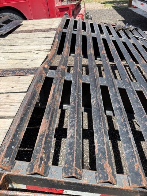 Black metal ramp with slotted treads laid on a wooden trailer deck outdoors