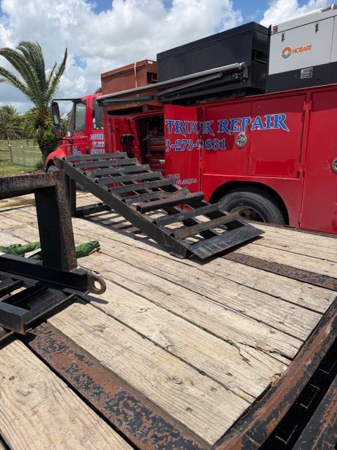 Red flatbed trailer with ramp next to a black truck in a sunny outdoor setting