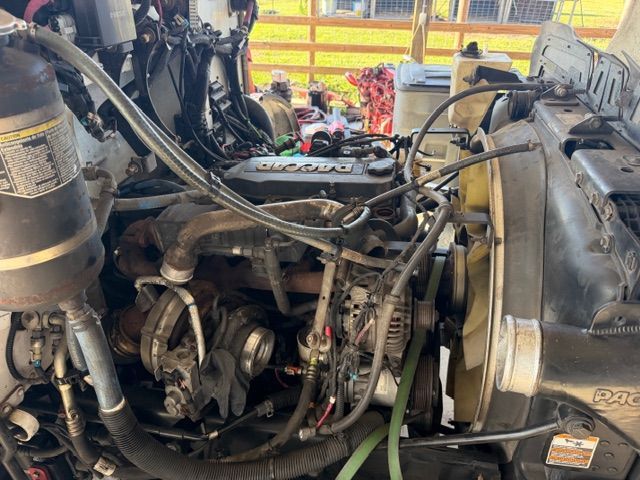 Dirty truck engine compartment with hoses, belts, and metal components visible under the hood