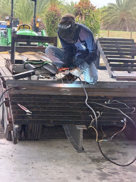 Person welding a metal bench frame outdoors, with tools and cables on a worktable.