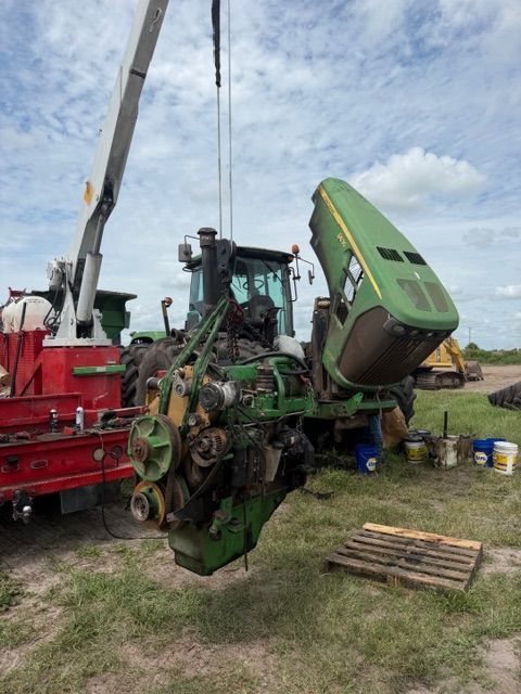 Farm machinery being repaired outdoors, with a green tractor/harvester tilted beside a red work truck.