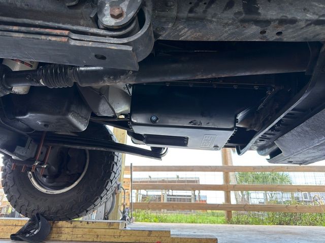 Underside of a lifted off-road vehicle with suspension and tire visible above a grassy field