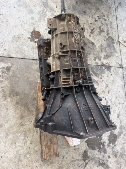 Broken black plastic transmission housing on a dirty concrete floor with a wooden block underneath