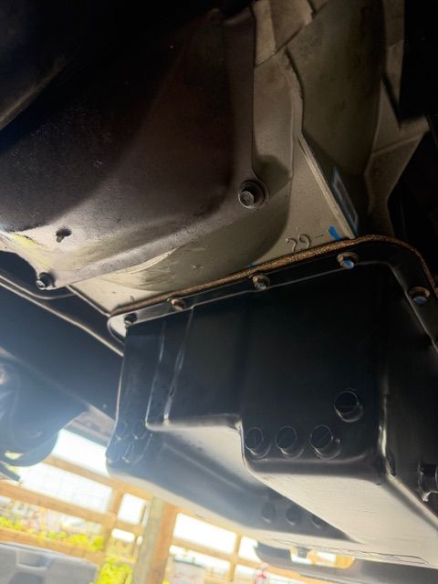Underside of a vehicle with a black metal undertray and visible bolts near the wheel well
