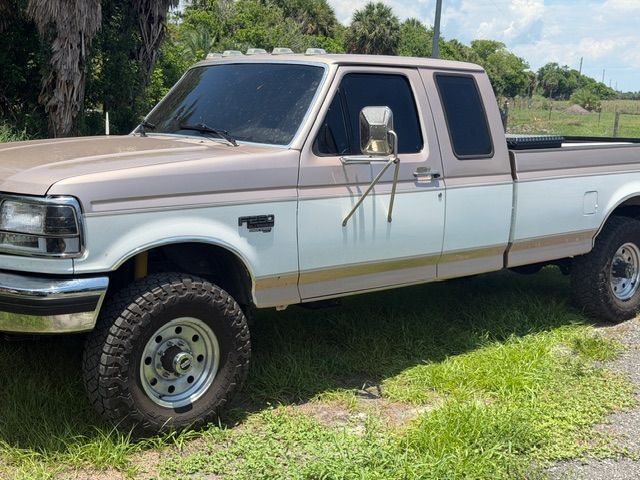 White extended-cab pickup truck parked on grass beside a road, with trees in the background
