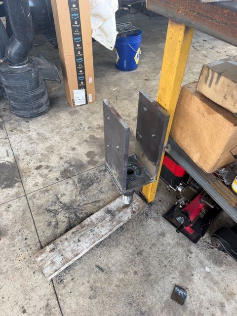 Workshop floor with metal brackets and a yellow support post beside tools and boxes