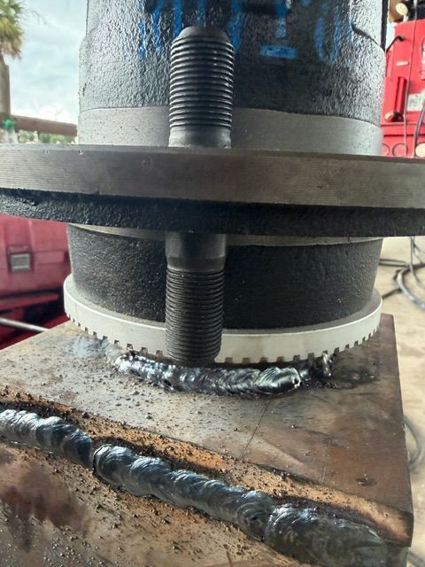 Close-up of a metal workpiece with threaded rods and weld beads on a rusted steel surface.