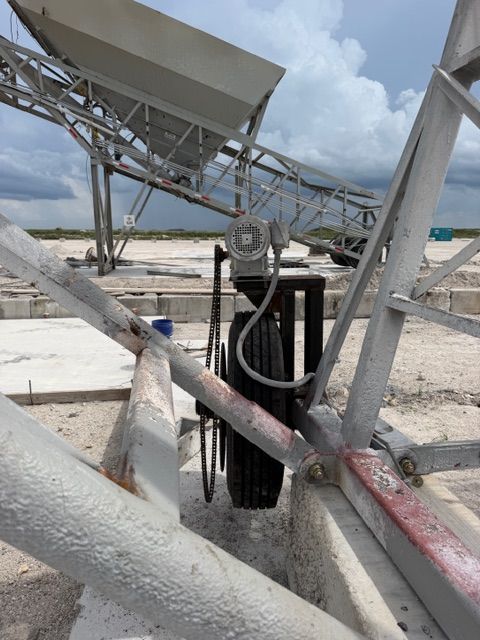 Industrial conveyor belt on a dusty rooftop under cloudy skies, with metal framework and cables.